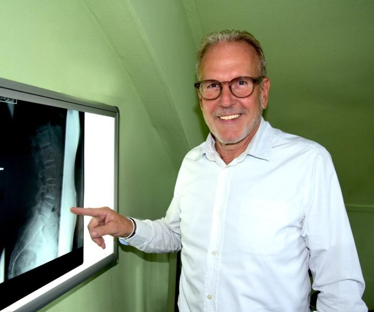 Ein Mann zeigt auf ein Röntgenbild der Wirbelsäule in einem Raum.
