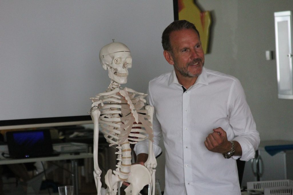 Ein Dozent präsentiert ein Skelettmodell in einem Unterrichtsraum.