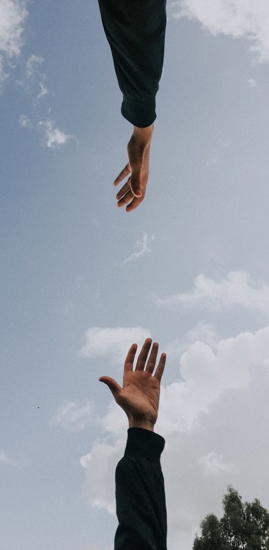 Gemeinsames Coaching Zwei Hände strecken sich zueinander gegen einen wolkigen Himmel.